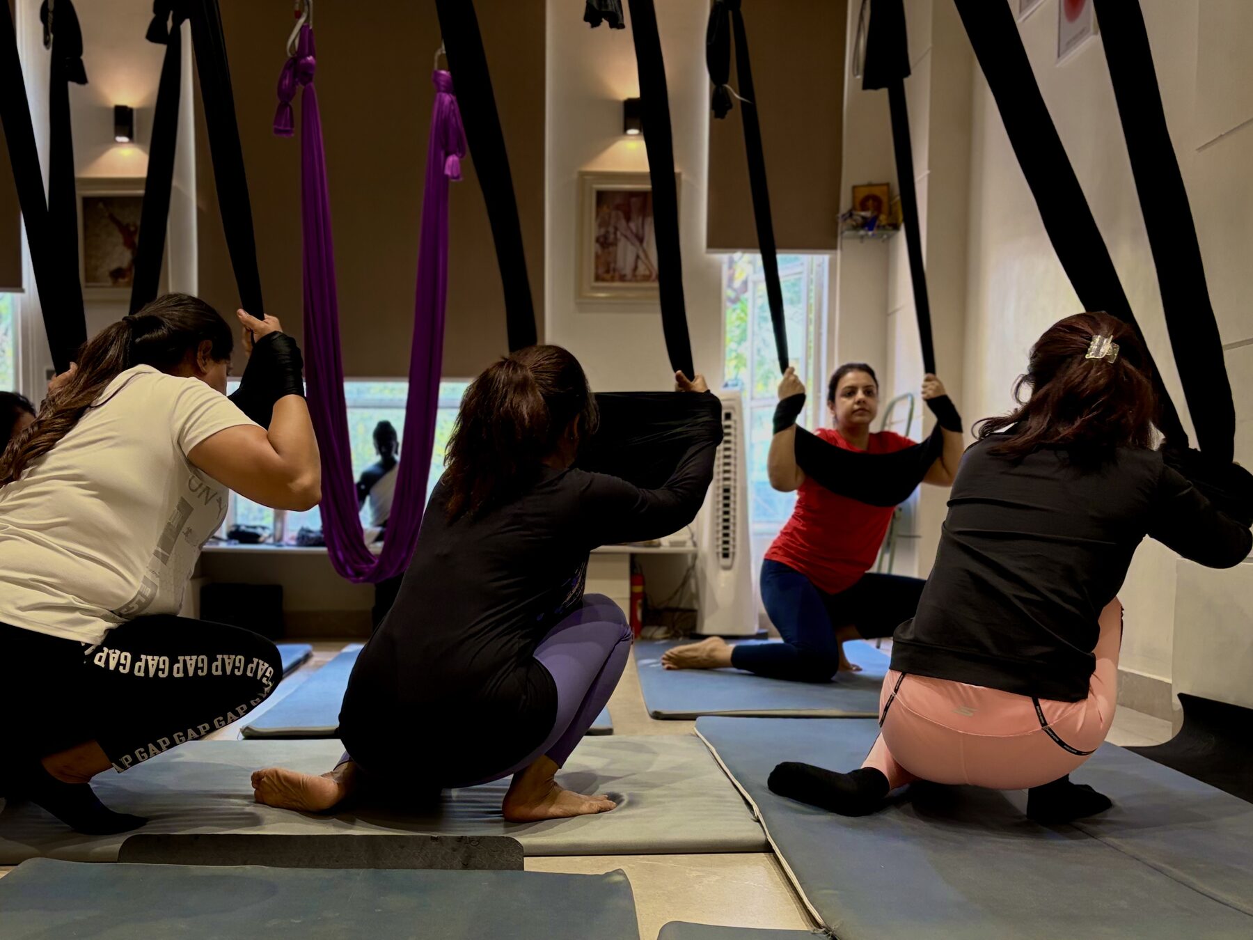 An aerial yoga class in the Aerial Divya studio, students working with black and purple hammocks
